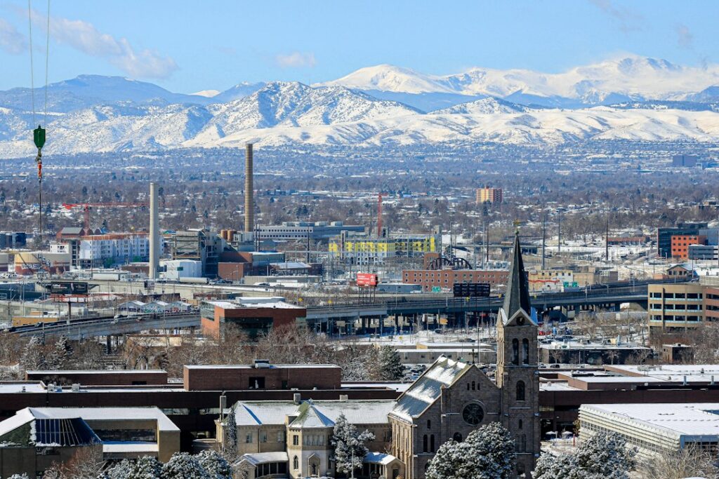 Snow on rooftops in Denver with the snow-covered Front Range mountains behind the city