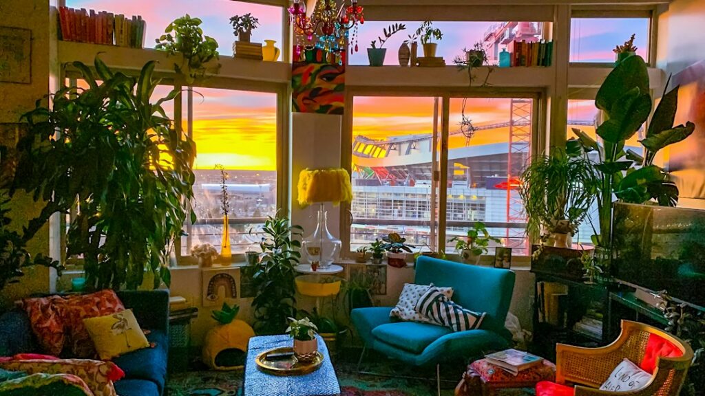 Plant-filled Denver apartment interior with a window view toward Mile High Stadium at sunrise