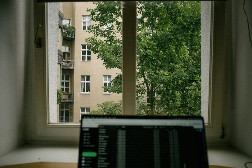 Laptop open in front of a window overlooking an apartment building